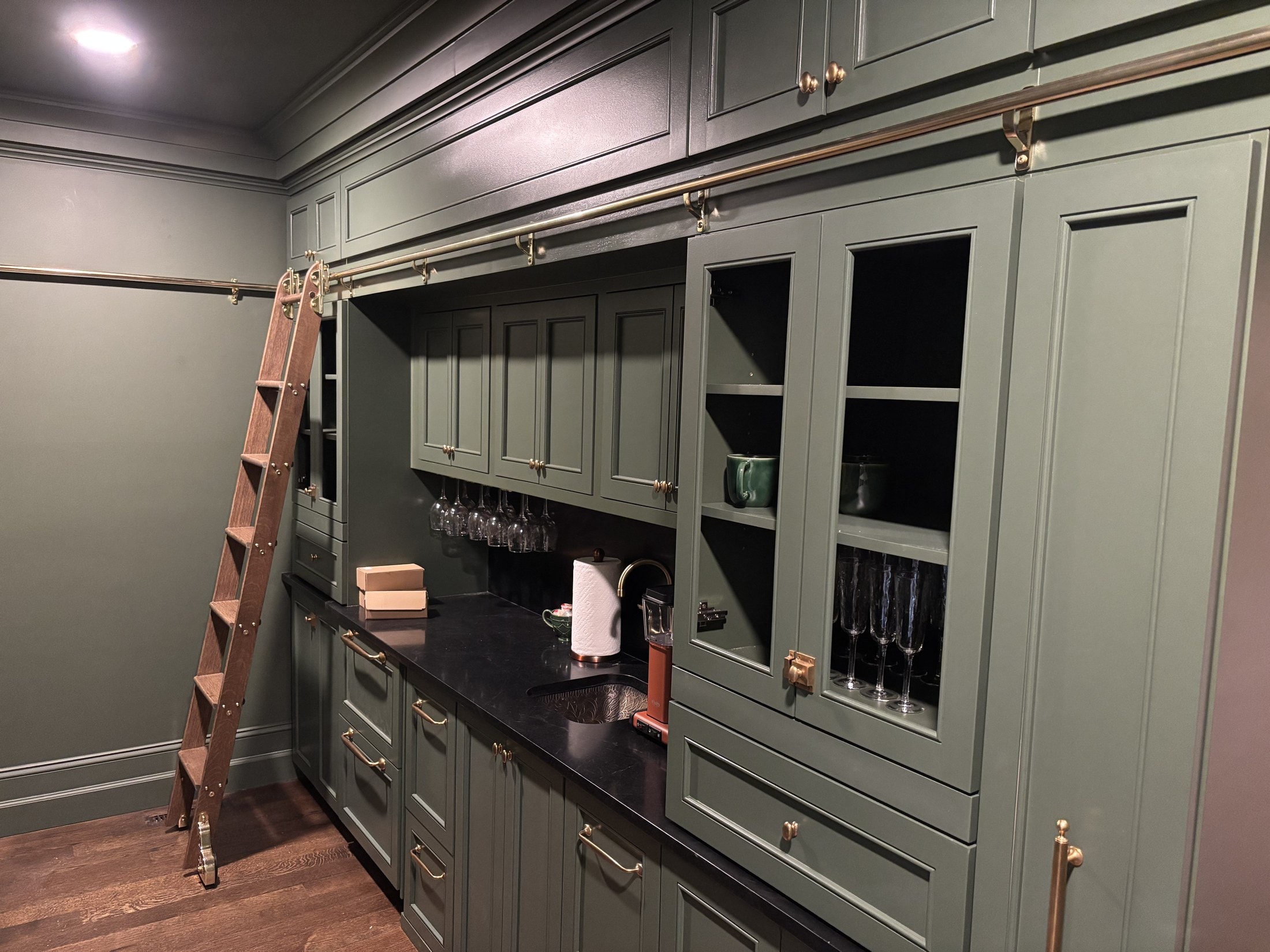 Sage-green butler's pantry with brass library ladder and glass-front cabinets