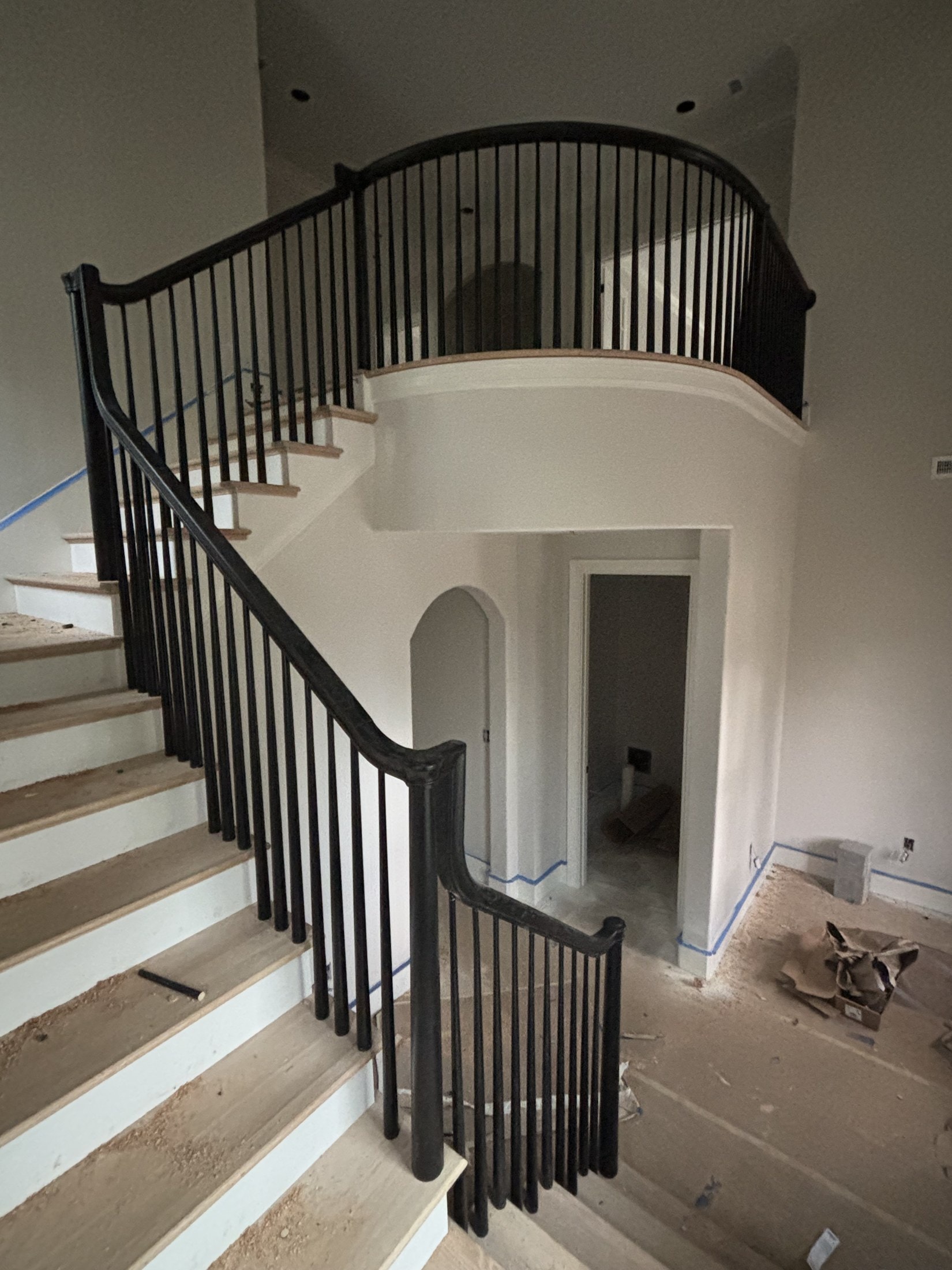 Curved staircase with black metal balusters and dark oak handrail mid-install