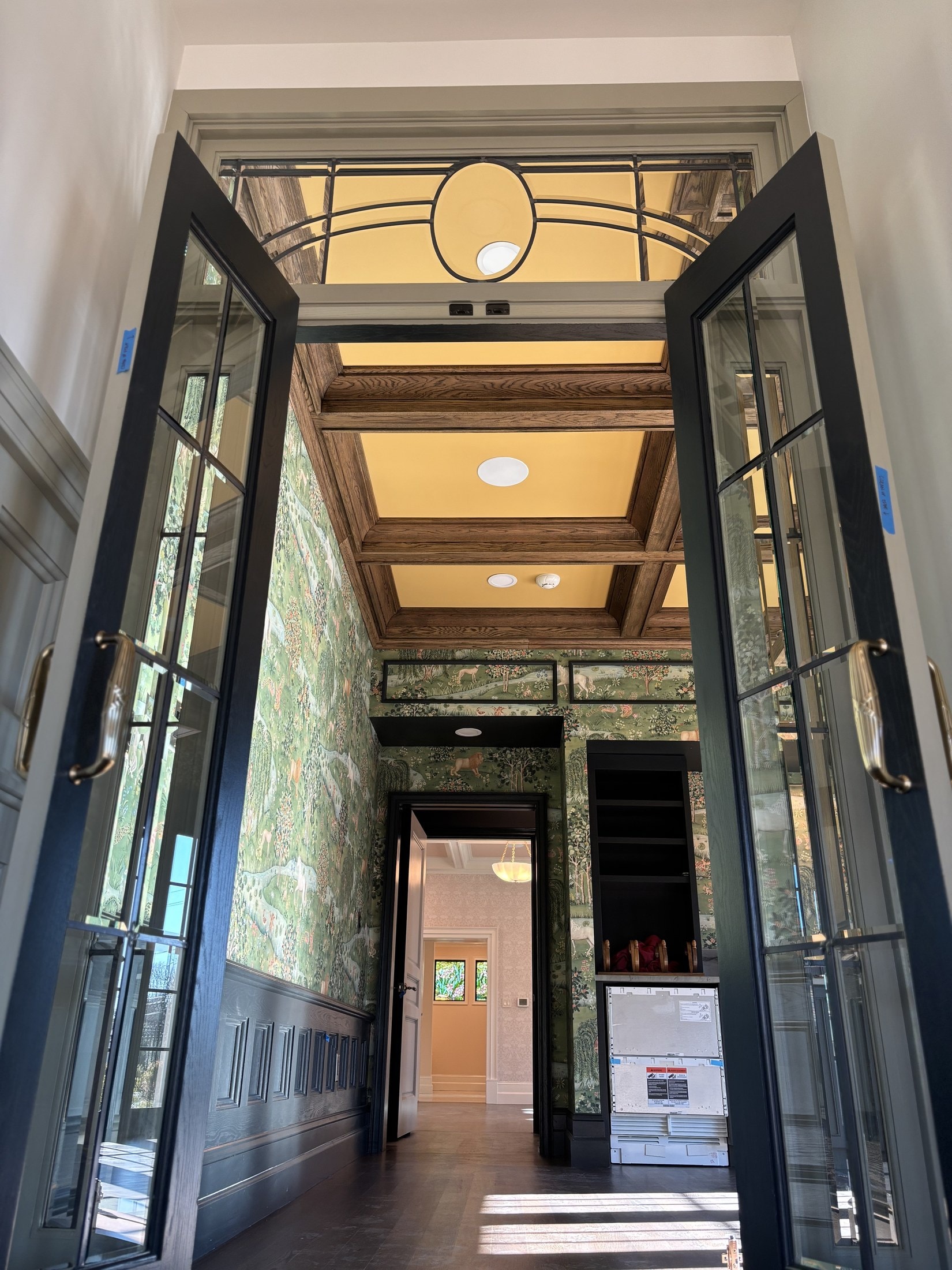 Double-door entry foyer with coffered ceiling, paneled wainscot, and botanical wallpaper