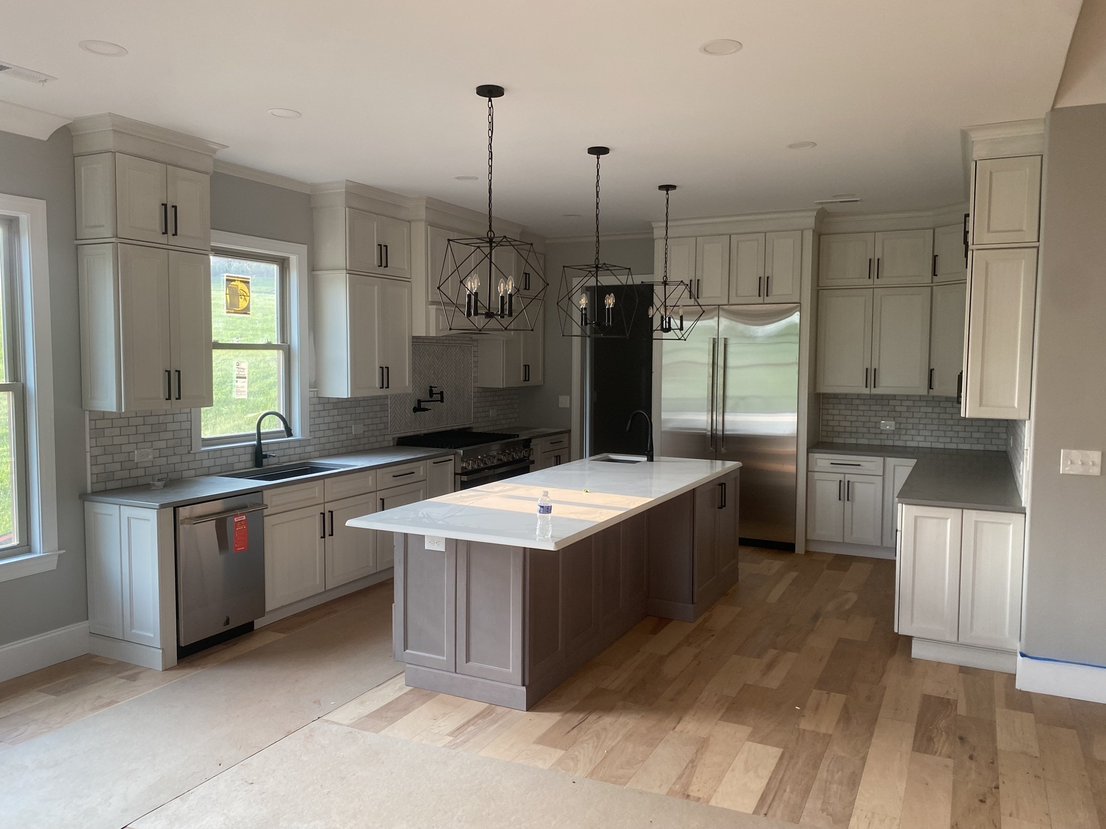 Kitchen with white shaker cabinets and wide-plank floors near completion