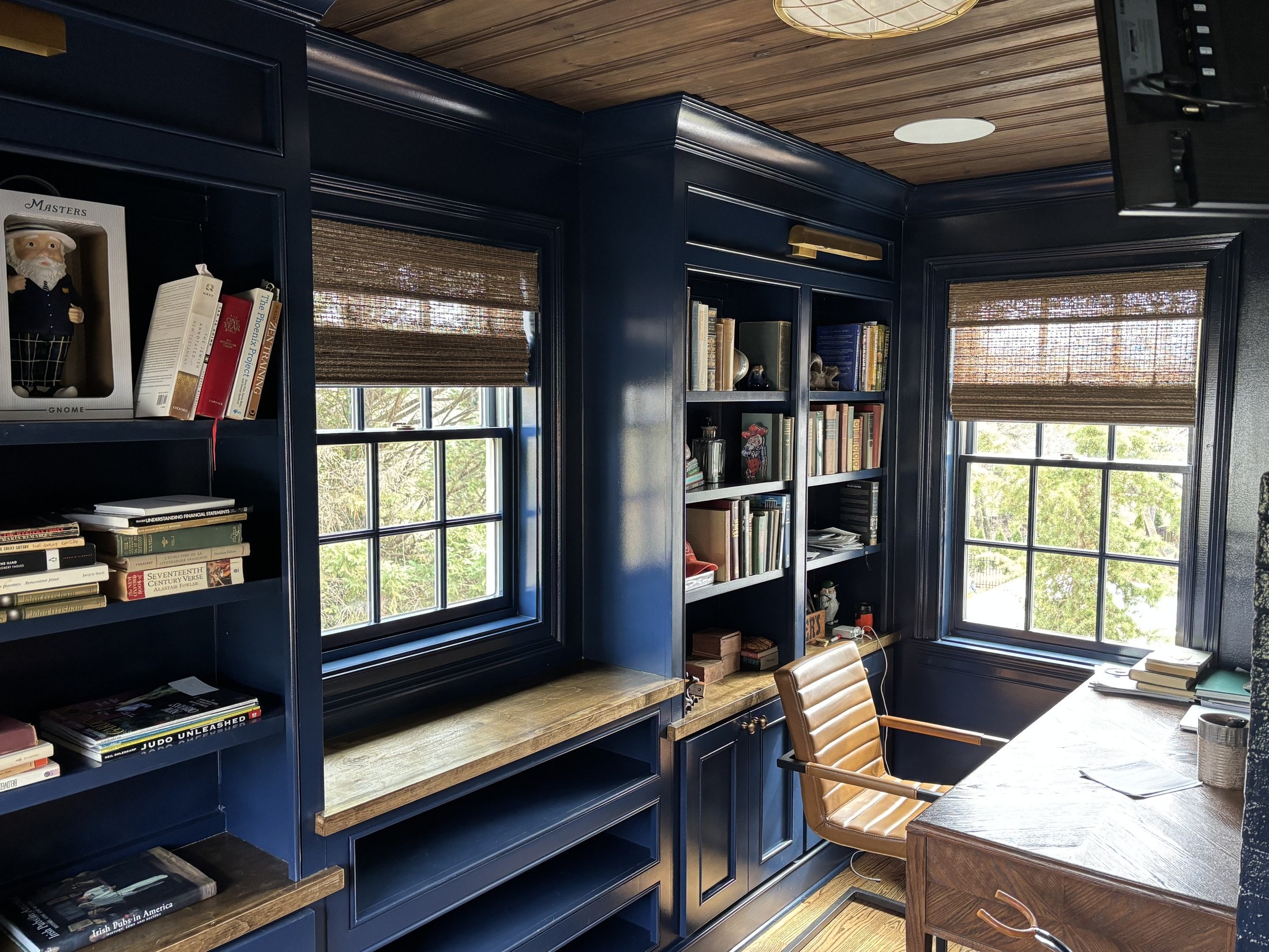 Navy-painted home library with built-in bookcases, window seats, and an oak desk