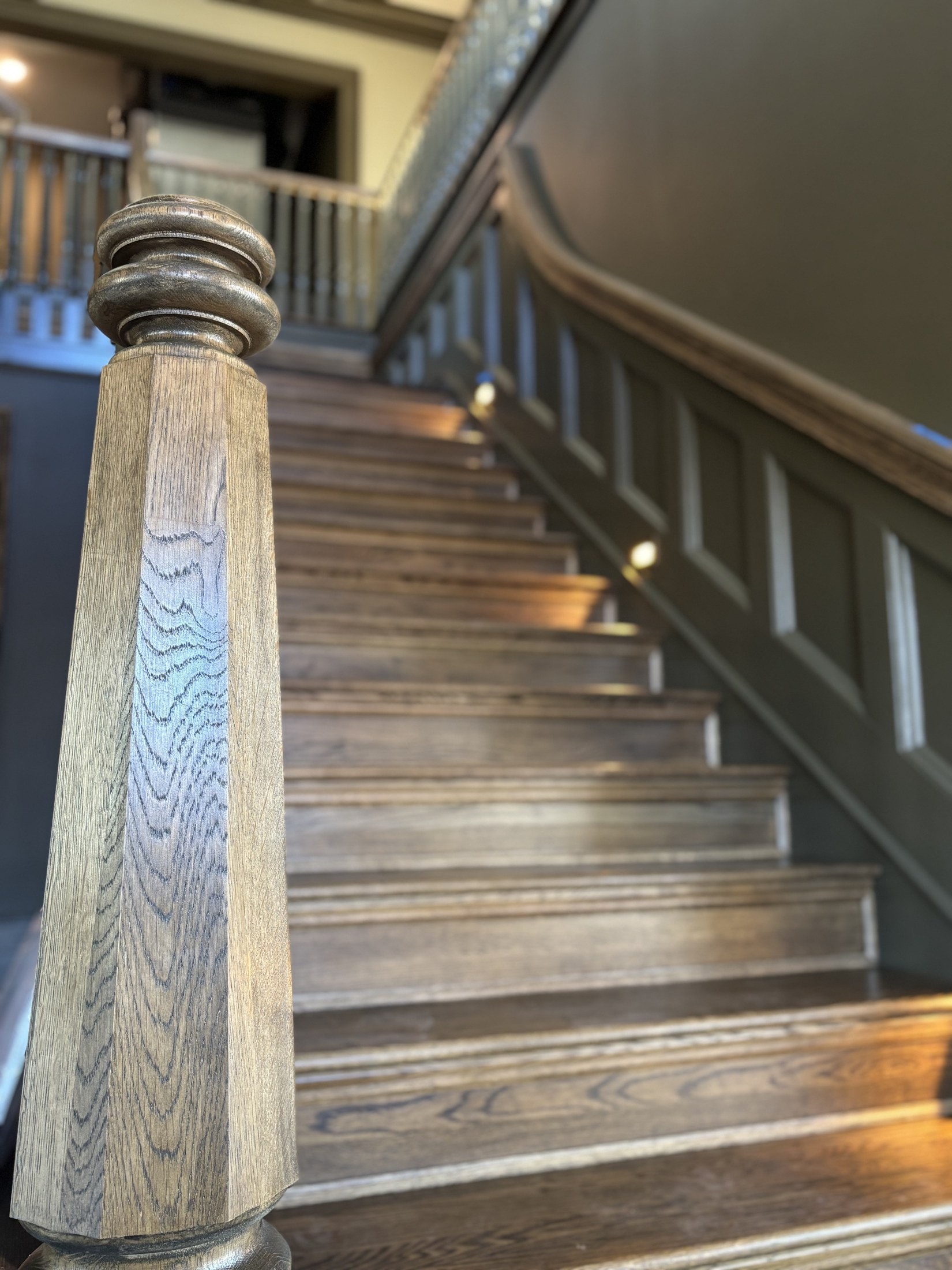 Hand-turned stained oak newel post on a staircase with paneled wainscot