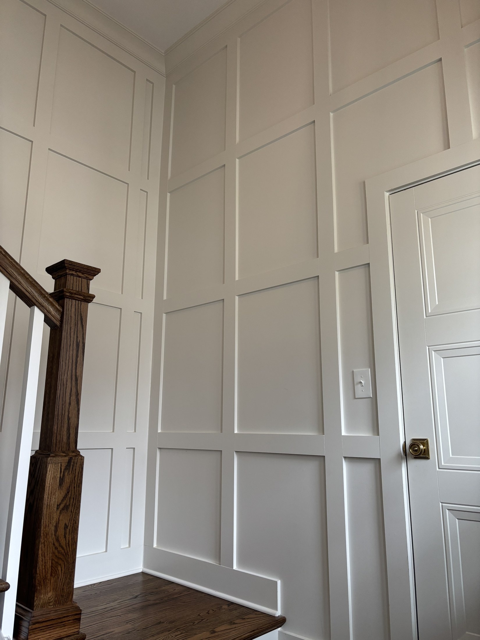 Picture-frame wainscoting on a tall stair wall with oak newel post